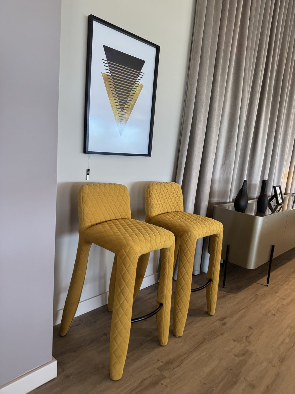 Interior con dos taburetes mostaza y una lámina gráfica enmarcada sobre pared clara
